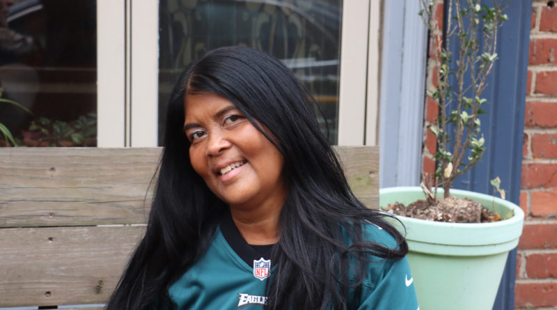 A woman wearing an Eagles shirt sits in front of her house.