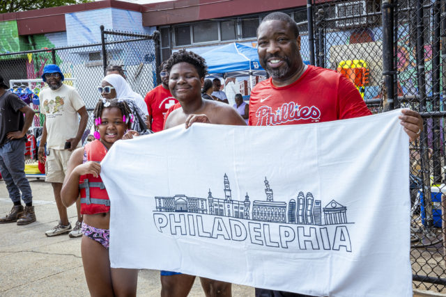 City Council President Kenyatta Johnson and youth hold up a Philadelphia Parks & Recreation towel after jumping in the pool. 