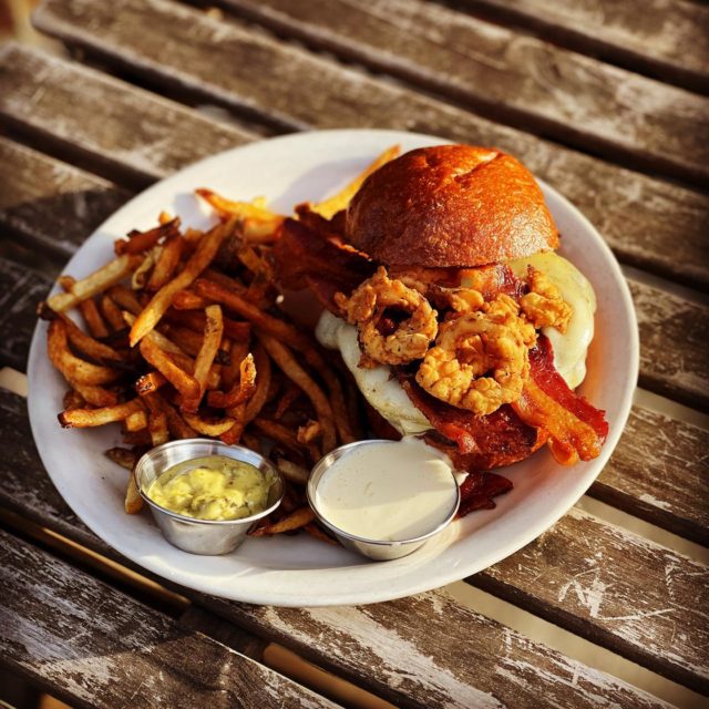 Watkins Drinkery's "Watkins burger" is 1/2 lb signature beef blend with crispy shallots, horseradish aioli, on a brioche bun.