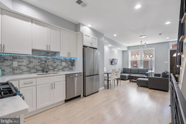 The interior of the first floor rowhouse. It shows a view of the kitchen into the living room. The kitchen features stainless steal appliances and white cabinets.