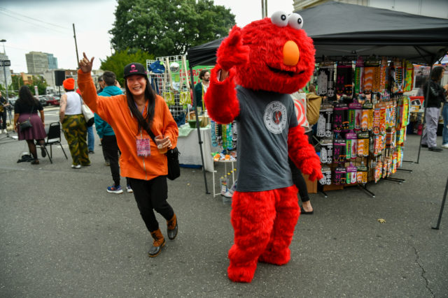 Philly AIDS Thrift mascot and a young woman wave to people walking by at the Philly AIDS Thrift annual block party and street festival in 2023.