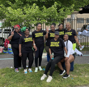 Members of the Double Dutch club gather for a photo in the park. They are all African-American women. Most of them are wearing a black T-shirt that says Double Dutch Meetup in bright yellow letters.