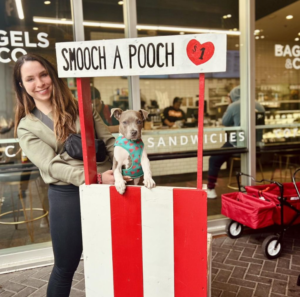 A woman holds a puppy at a both that says Smooch A Pooch. The booth is made of wood and painted red and white.